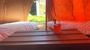 Une tente avec deux lits, une fenêtre et un seau rouge posé sur le rebord de la fenêtre.