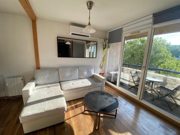A modern living room with a white sofa, a small round table, a ceiling fan, and a large sliding glass door leading to an outdoor area with a table and chairs.