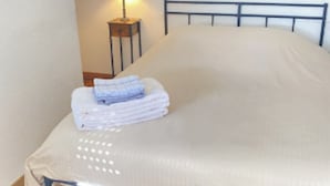 A single bed with a metal frame, a bedside table with a lamp, and a folded towel on the bed.