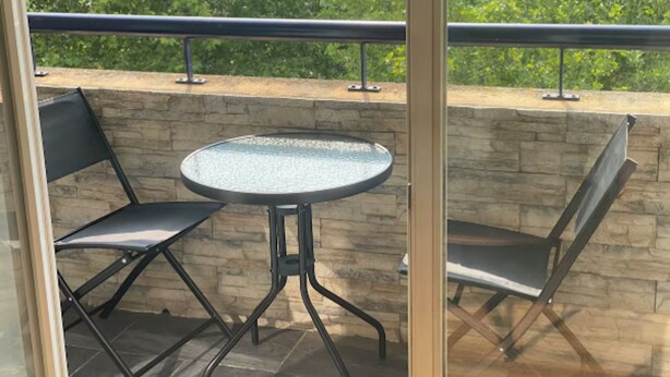A balcony with a round table and two chairs, a stone wall, and a metal railing.