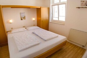 Een eenpersoonsbed met houten hoofdbord, twee bedlampjes, een raam en een radiator.