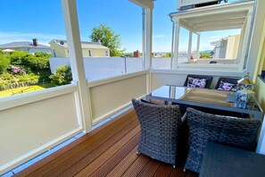 Een balkon met een houten vloer, rieten meubels en een glazen tafel.