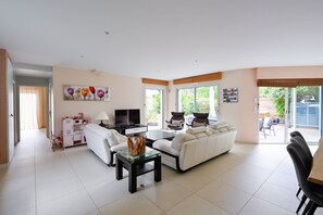 A modern living room with a sofa, a coffee table, a TV, and a dining area with chairs. - Ker Augusta - Jolie maison 4 chambres avec piscine (Mesquer)