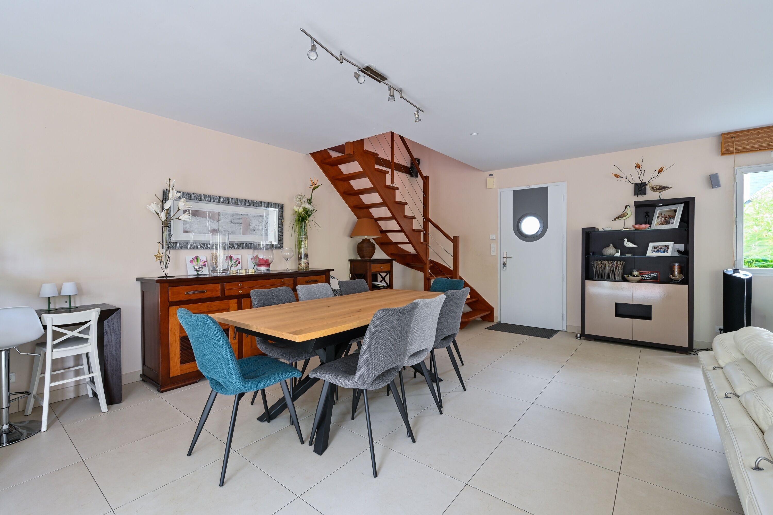 A modern kitchen with a wooden dining table, grey chairs, a built-in stove, and a wooden staircase.