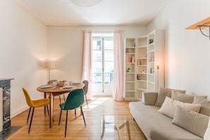 A living room with a sofa, a dining table with chairs, a bookshelf, and a window with curtains. - Opaline - Bel appt 2 chambres au cœur de Nantes (Nantes)