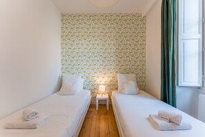 Ein kleines, gemütliches Schlafzimmer mit zwei Einzelbetten, einem Nachttisch, einer Lampe und einem Fenster mit Vorhängen.