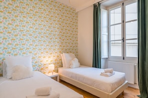 A hotel room with two beds, a window with curtains, and a patterned wallpaper. - Opaline - Bel appt 2 chambres au cœur de Nantes (Nantes)