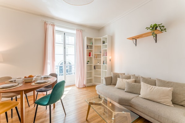 A living room with a sofa, a dining table with chairs, and a bookshelf. - Opaline - Bel appt 2 chambres au cœur de Nantes (Nantes)