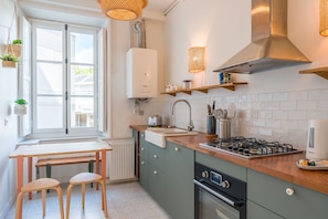 Et moderne køkken med gaskomfur, ovn og et vindue med skodder.