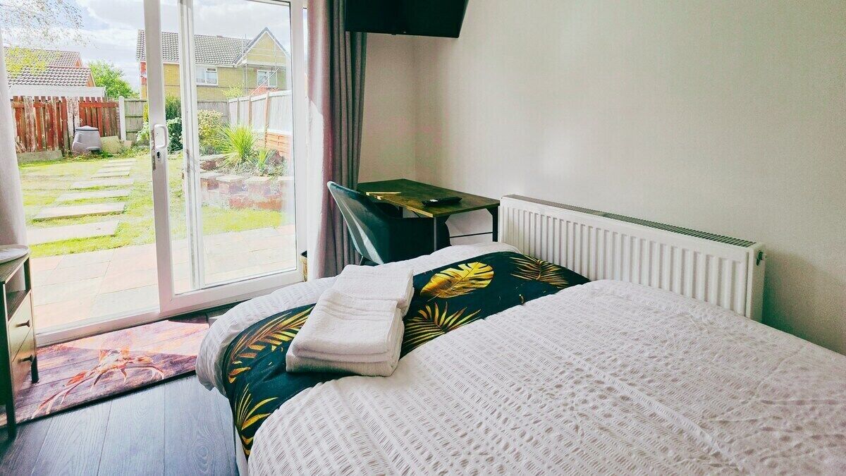 A bedroom with a bed, a desk, and a view of the garden through a sliding door.