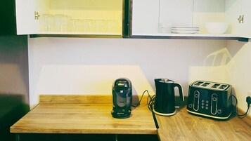 Una kitchenette con cafetera, hervidor y tostadora sobre una encimera de madera.