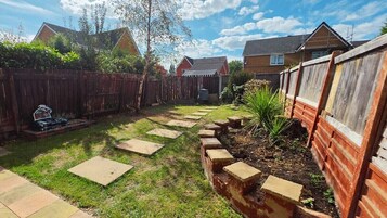A backyard with a wooden fence, stepping stones, and a garden area.