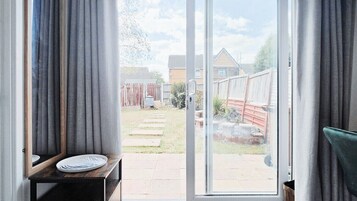A room with a sliding glass door leading to a backyard with a wooden fence, a bench, and a small garden area.