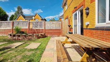 Un patio trasero con un banco de madera, un muro de ladrillo y un área cercada.
