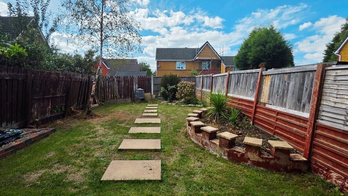 A backyard with a wooden fence, a pathway, and a house in the background.