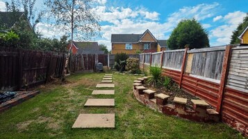 Un patio trasero con cerca de madera, un sendero y una casa al fondo.