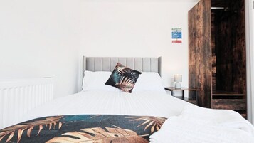 A bedroom with a bed, a nightstand, a lamp, and a door.
