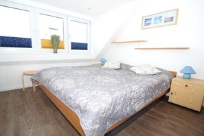 Un dormitorio con cama, mesitas de noche, una ventana con persianas y un estante en la pared.