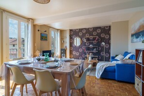 A dining area with a table set for four, a blue sofa, and a bookshelf. - L’Écrin de Limoges - Grand studio avec parking (Limoges)