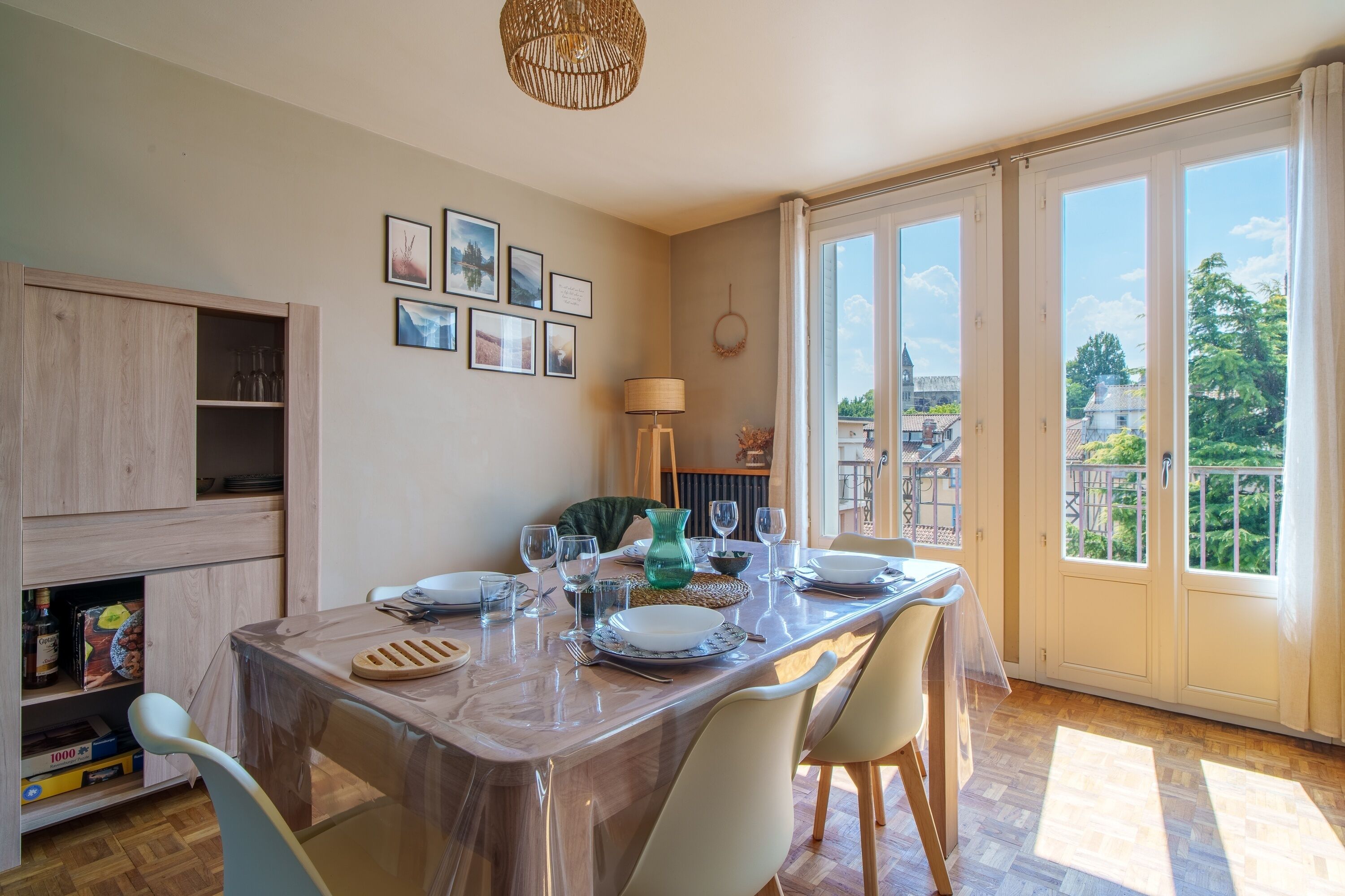 A dining area with a table set for four, a wooden cabinet, and a view of the city through large windows.