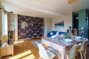 Ein Essbereich mit einem Marmortisch, weißen Stühlen und einem blauen Sofa im Hintergrund.
