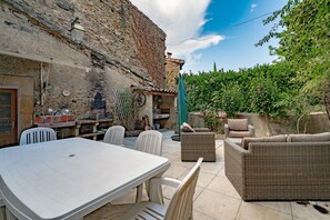 Una terrazza esterna con tavolo e sedie, un divano in vimini e un muro in pietra.