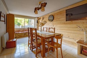 Un'area pranzo con tavolo e sedie in legno, una sveglia appesa al muro e una finestra vista sul verde.
