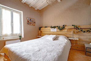A bedroom with a large bed, wooden headboard, bedside tables, a window with curtains, and a wall-mounted photo collage.