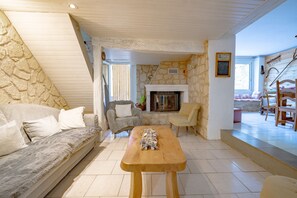 A cozy living room with a stone wall, a fireplace, a wooden table, and a sofa.