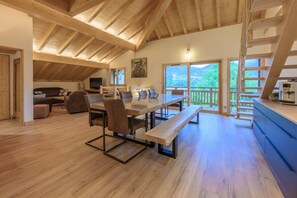 A spacious living area with a wooden ceiling, a dining table with chairs, a sofa, a TV, and a painting on the wall. - Chalet Adenore - Triplex proche des pistes (Samoëns)