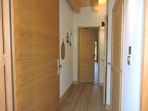 A hallway with wooden flooring and doors, leading to a room with a view of the outdoors. - Chalet Adenore - Triplex proche des pistes (Samoëns)
