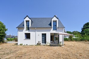 A two-story house with a sloped roof, a front porch with a table and chairs, and a large window. - Ty Liv - Maison familiale avec un beau jardin (Saint-Gildas-de-Rhuys)