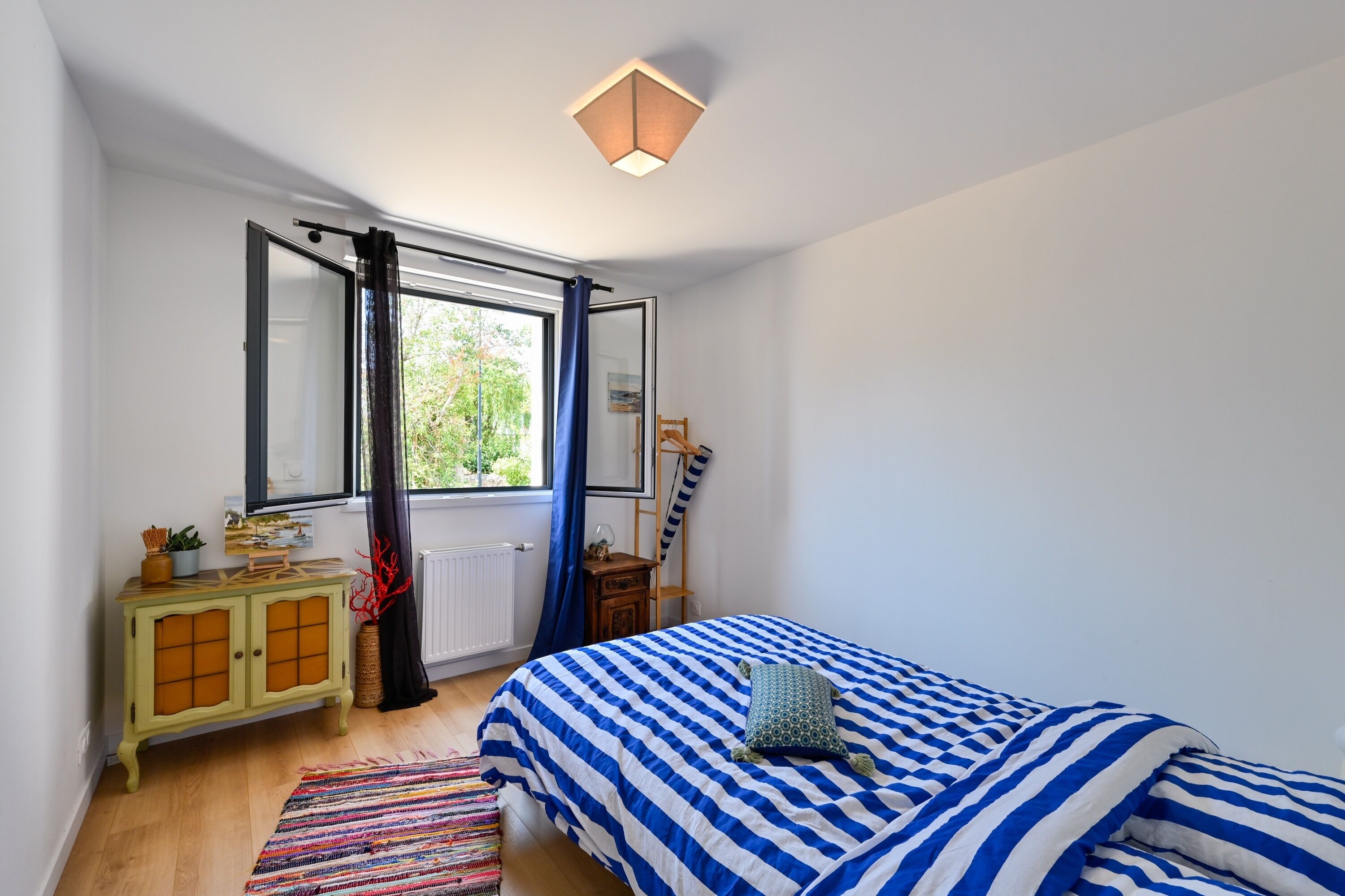Quarto com cama, janela, radiador, armário e cadeira suspensa.
