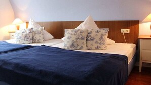 A bed with a blue bedspread and floral pillows, a wooden headboard, and bedside lamps. - Bötticher Str. 6 Holiday Apartment 3 (Sylt \/ OT Westerland)