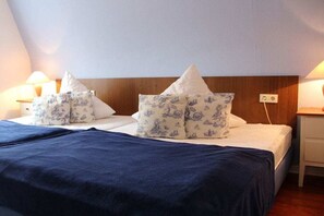 Una cama con colcha azul y almohadas estampadas, cabecera de madera y lámparas de noche.