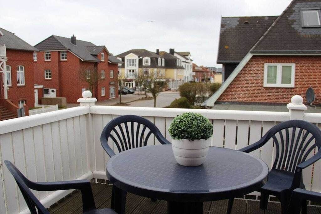 A balcony with a round table and chairs, a potted plant, and a white railing.