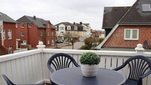 A balcony with a round table and chairs, a potted plant, and a white railing. - Bötticher Str. 6 Holiday Apartment 3 (Sylt \/ OT Westerland)