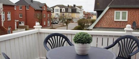 A balcony with a round table and chairs, a potted plant, and a white railing.