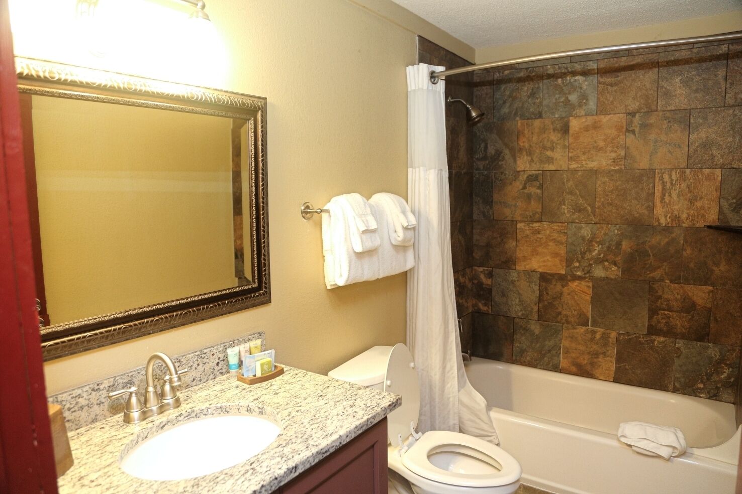 Une salle de bain avec un lavabo en marbre, des toilettes, une baignoire et un rideau de douche.