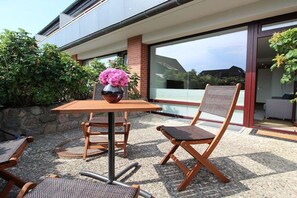 Un patio al aire libre con una mesa y sillas, un jarrón con flores y vistas a un edificio moderno.