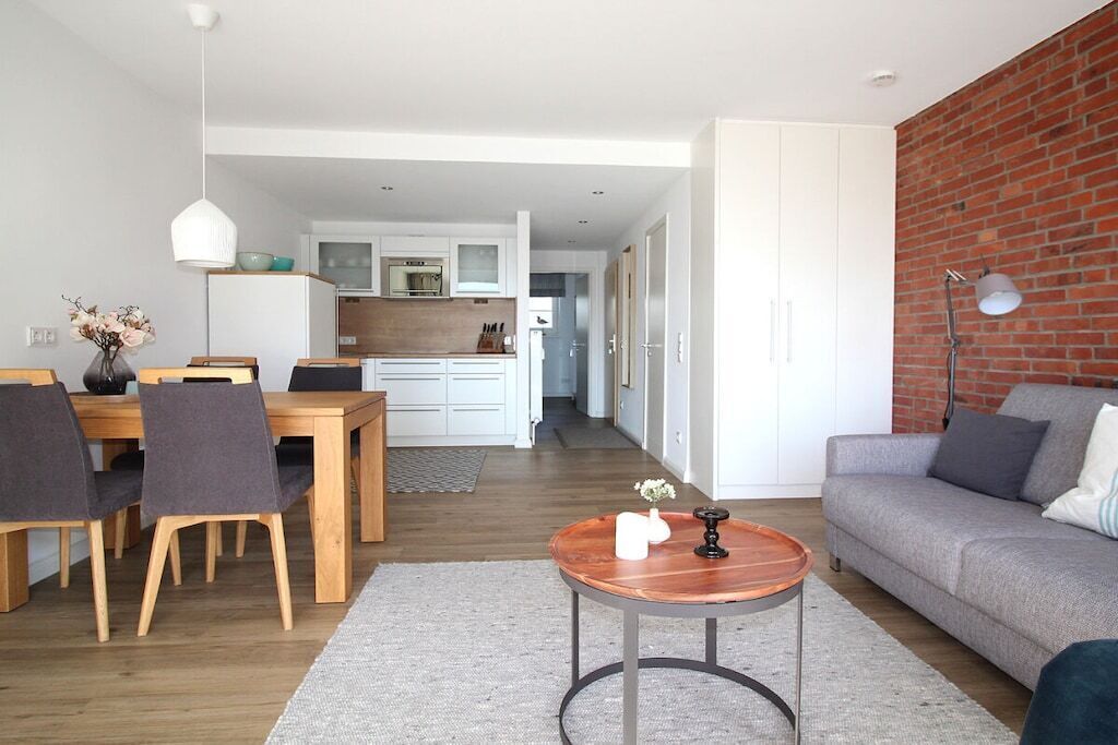 A modern living room with a dining area, a kitchen in the background, and a brick accent wall.
