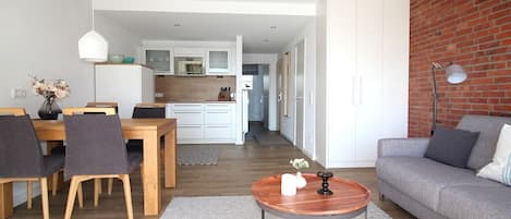 A modern living room with a dining area, a kitchen in the background, and a brick accent wall.