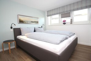 Un dormitorio con cama, mesita de noche, silla, ventana con vistas y un cuadro en la pared.