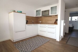 A compact kitchen with white cabinets, a microwave, and a sink. - Fischerweg 15i Ground Floor (Sylt \/ OT Westerland)