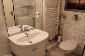Un baño con lavamanos blanco, espejo, inodoro y toallero.