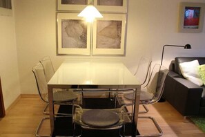 Un comedor con mesa y sillas de vidrio, una lámpara y un sofá con un cojín.