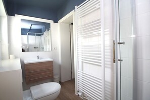 Un baño con inodoro blanco, tocador de madera, espejo y cabina de ducha de vidrio.