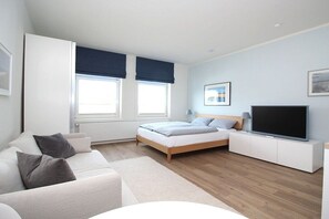 Un dormitorio moderno con cama, televisor, sofá y ventana con persianas.