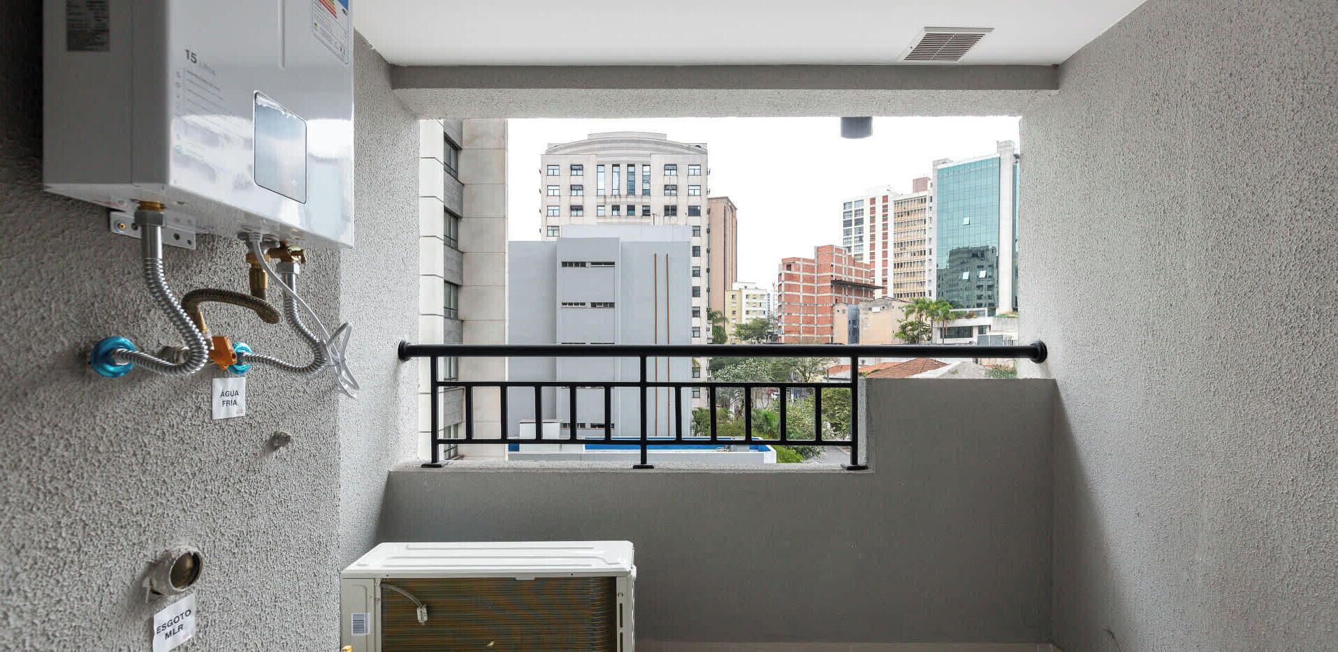 A balcony with a view of city buildings, a water heater, and a window with a metal railing.