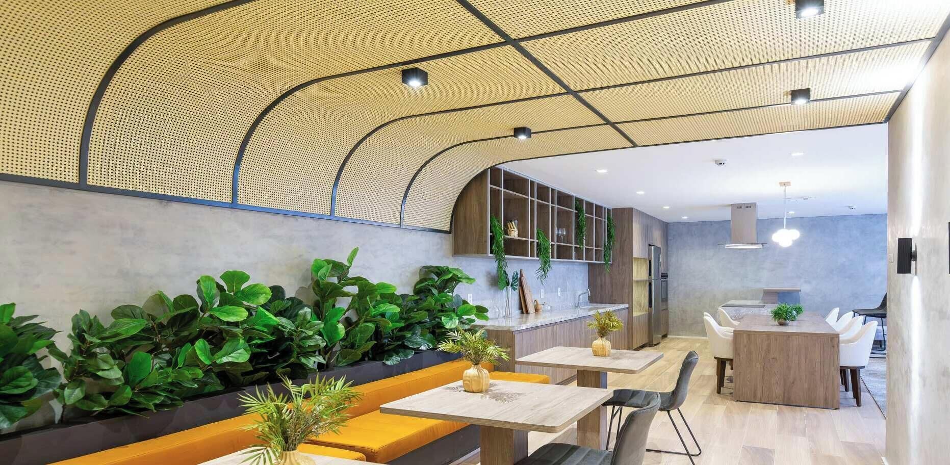 A modern interior with a curved ceiling, green plants, wooden seating, and a kitchen area.